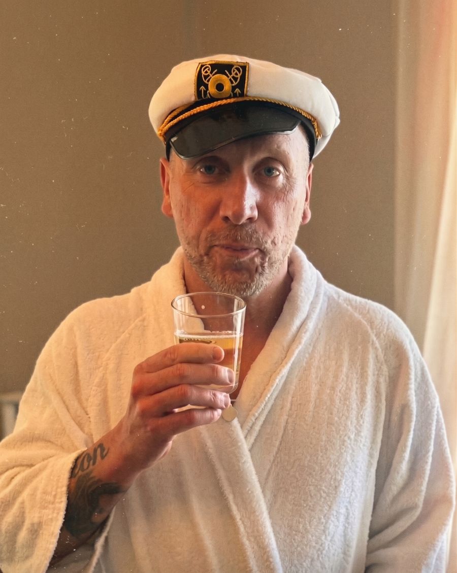 Henrik i kaptensmössa och morgonrock höjer ett glas