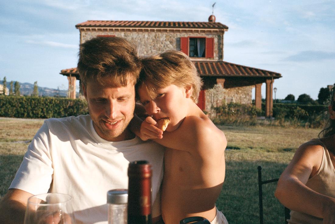 En pappa och en liten pojke kramas vid middagsbordet framför ett toskanskt stenhus