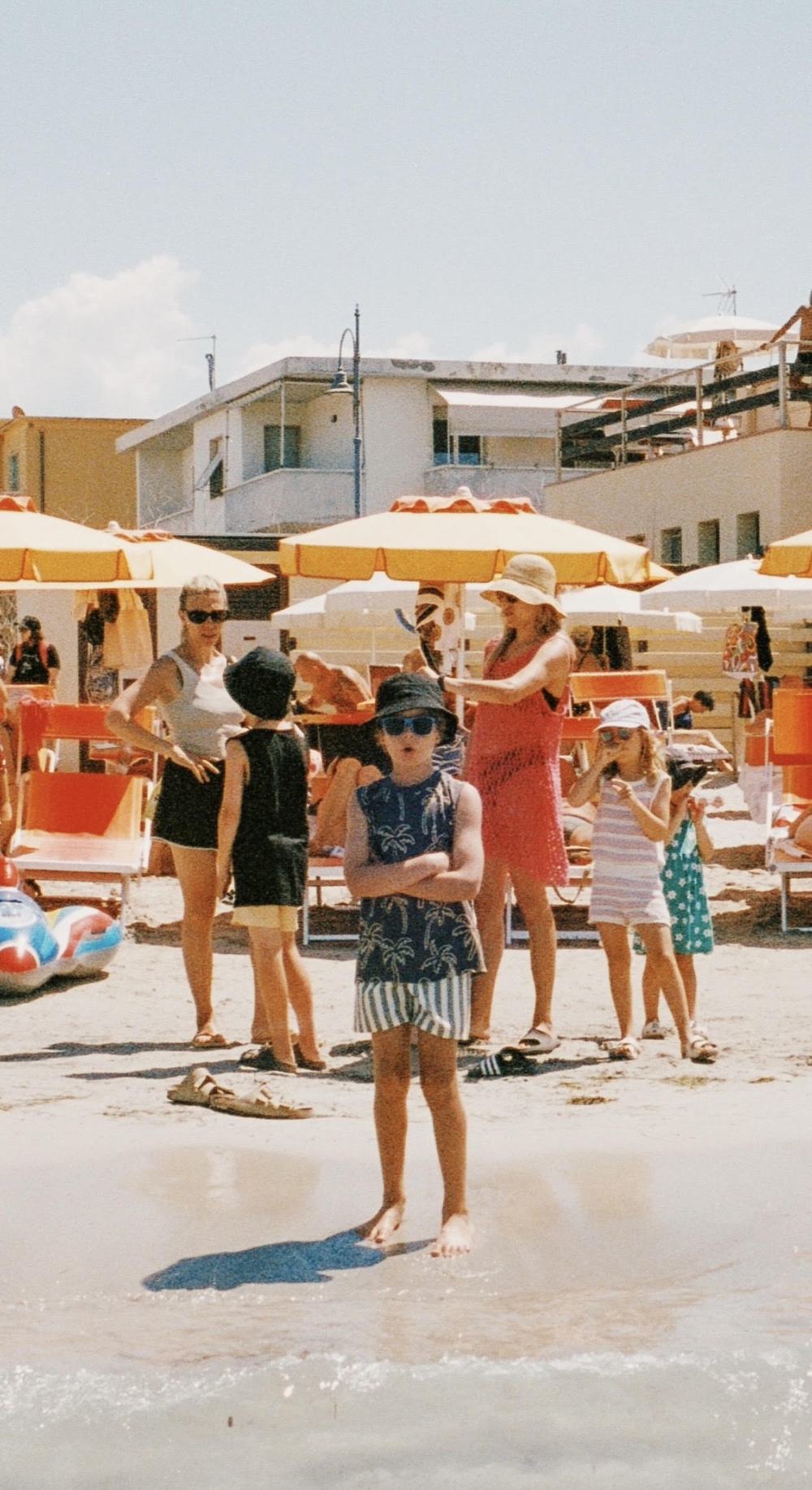 Barn och vuxna på en italiensk strand med gula parasoller